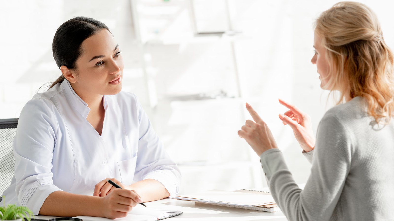 Contractura-capsular: dermatólogo sentado en la mesa y escuchando al paciente en la clínica