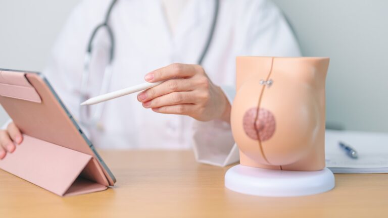 Una doctora explica la cirugía con un modelo anatómico de mama y una tableta