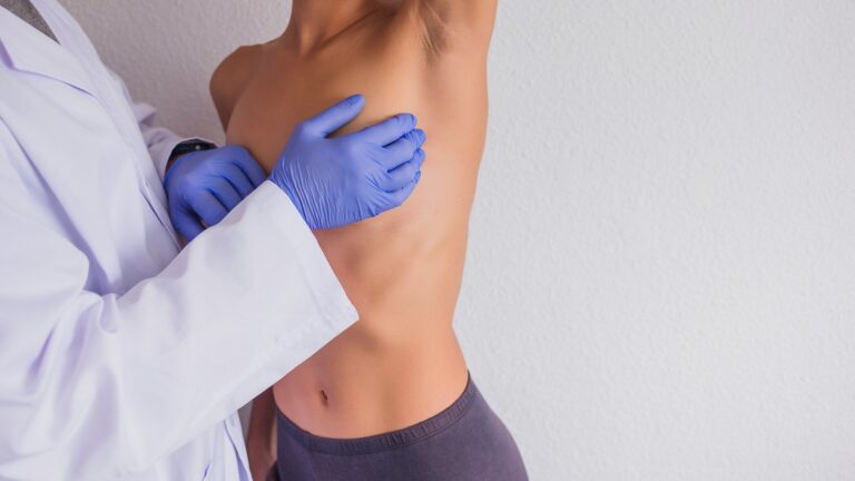 Exploración del pecho con guantes a una paciente de perfil con el brazo levantado