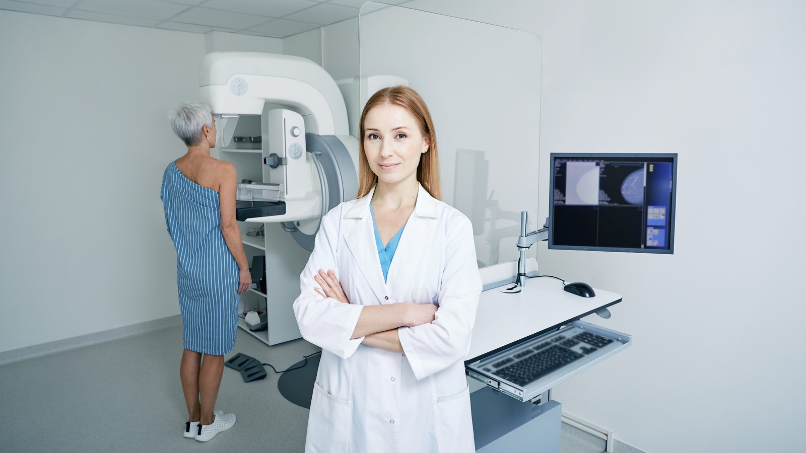 Mamografia con implantes: retrato de mamólogo con los brazos cruzados de pie en la sala de radiología con máquina de imágenes para