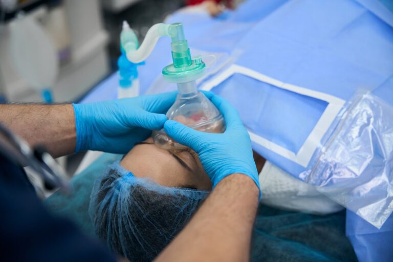 Un anestesista con guantes sujeta la mascarilla de anestesia a una paciente tumbada en el quirófano